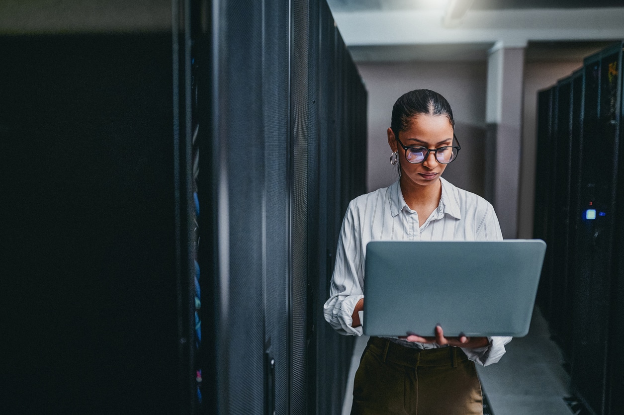 This is an image: female worker is in a cloud server room, looking at a large tablet