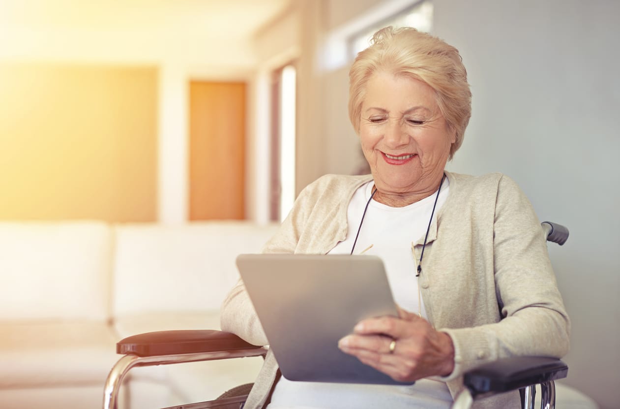 This is an image of an elderly woman sitting in a wheelchair using a digital tablet.